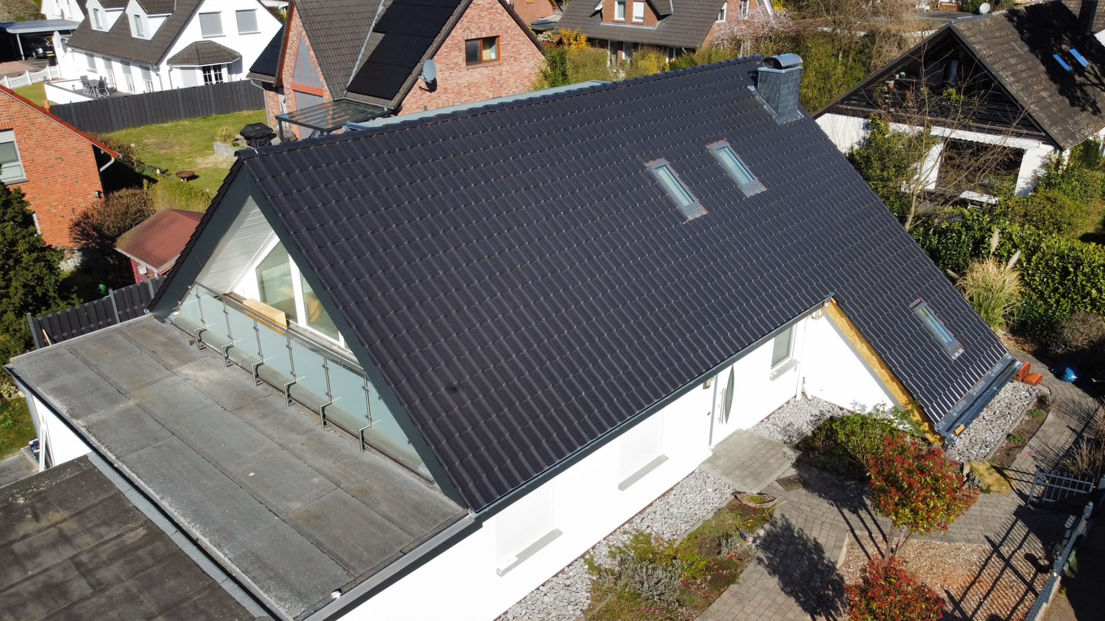 Fertig gedecktes Steildach mit anthrazitfarbenen Ziegeln, zwei Dachflächenfenstern, Schornstein und Loggia