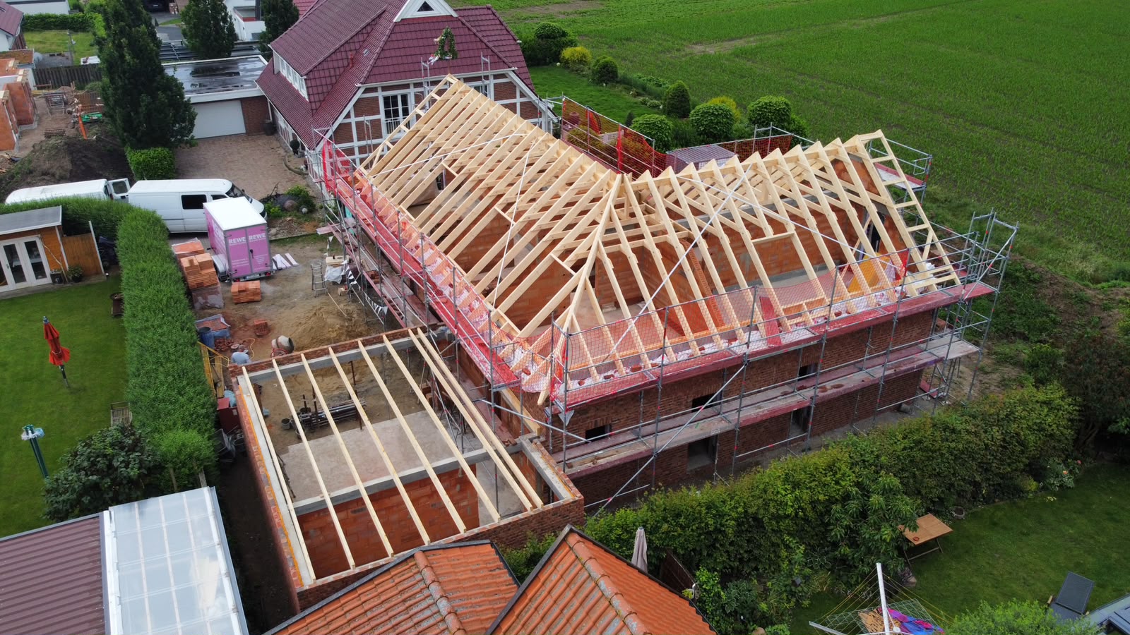 Luftaufnahme eines Rohbaus aus rotem Klinker mit frisch aufgerichtetem, noch ungedecktem Dachstuhl aus hellem Holz