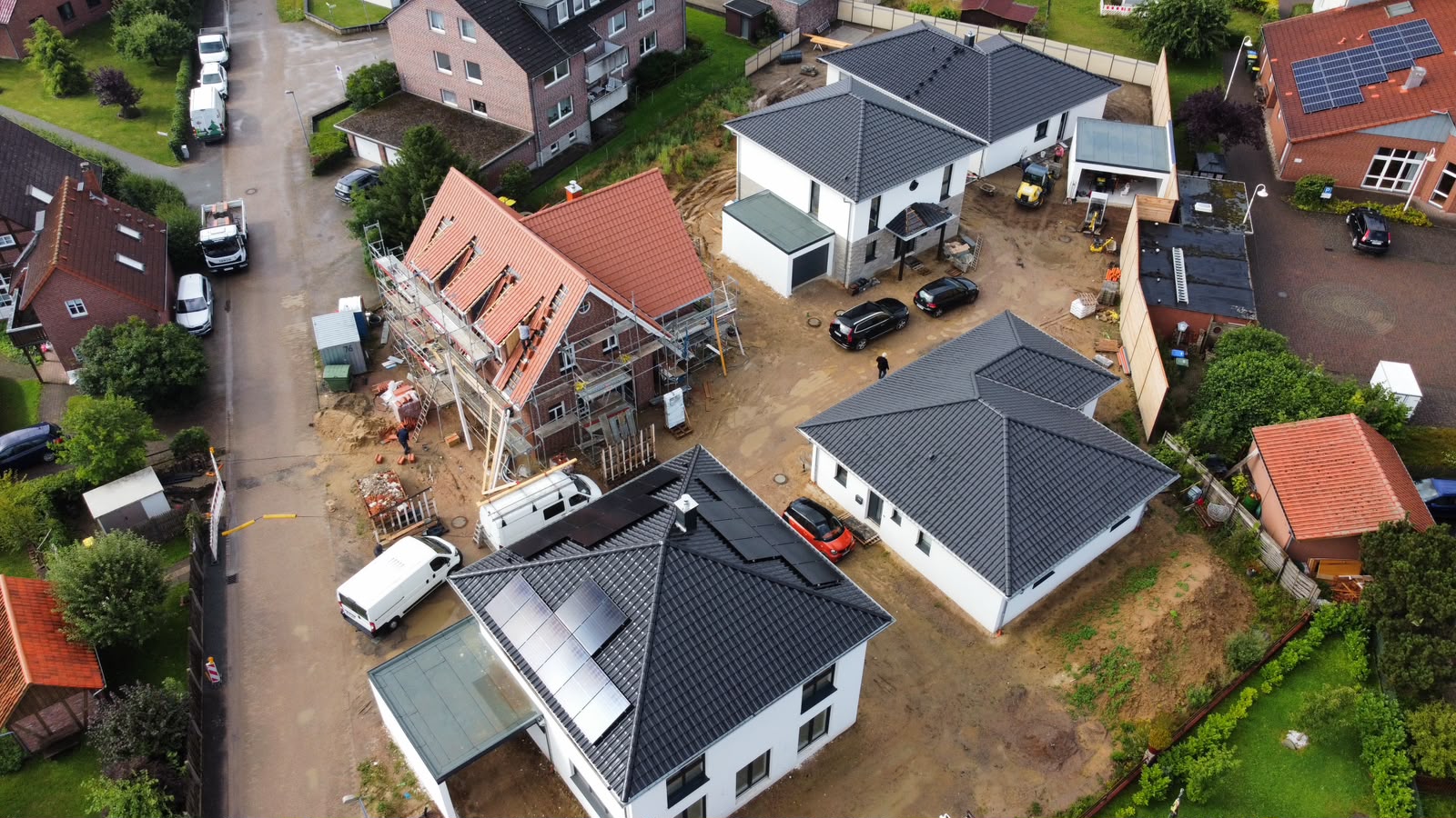 Luftaufnahme eines Neubauareals mit fertig gestellten weiß verputzten Häusern, anthrazitfarbenen Walmdächern und Photovoltaikanlagen
