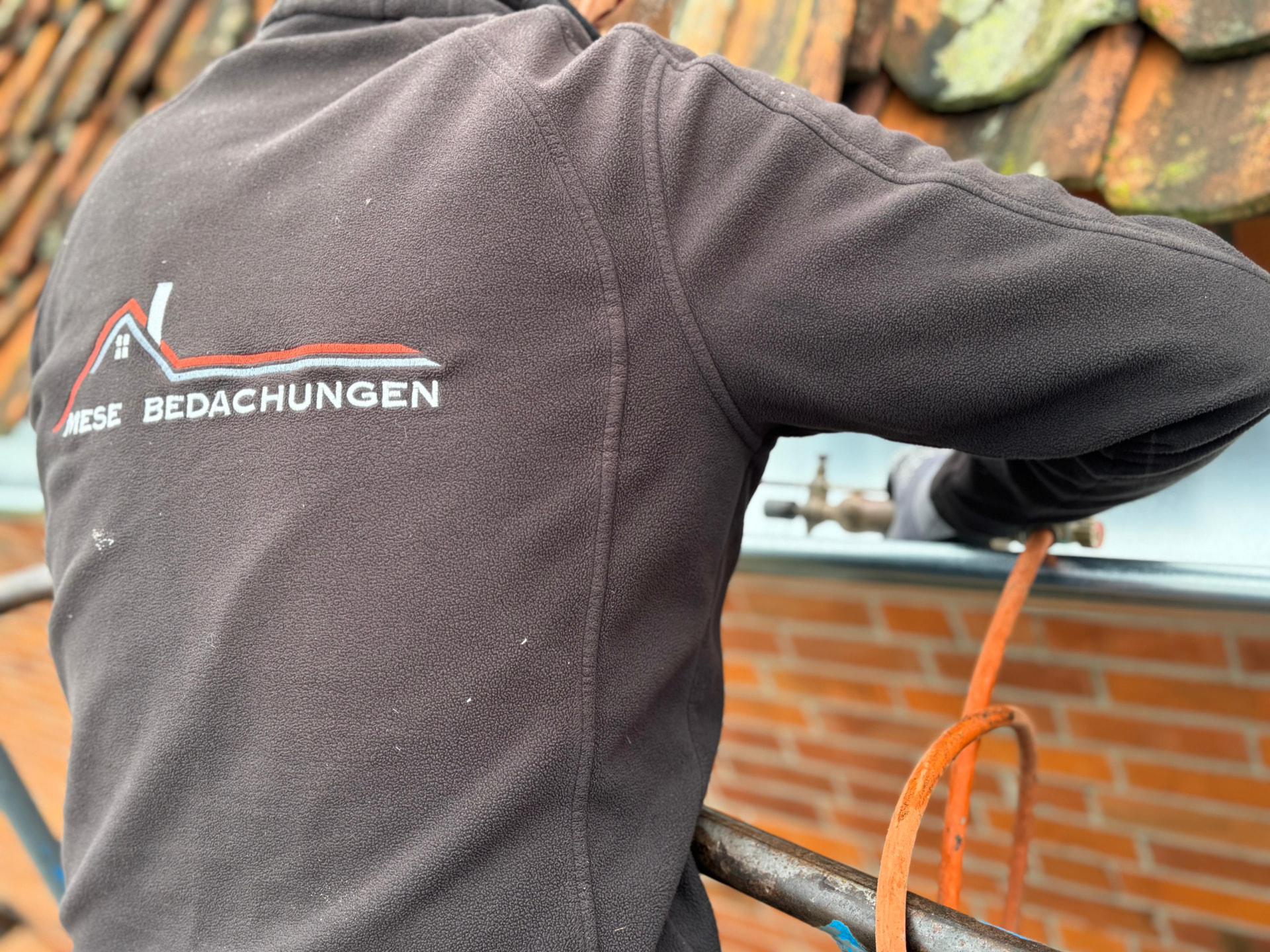 Dachdecker von Mese Bedachungen lotet eine Zink-Dachrinne an einer Klinkerfassade