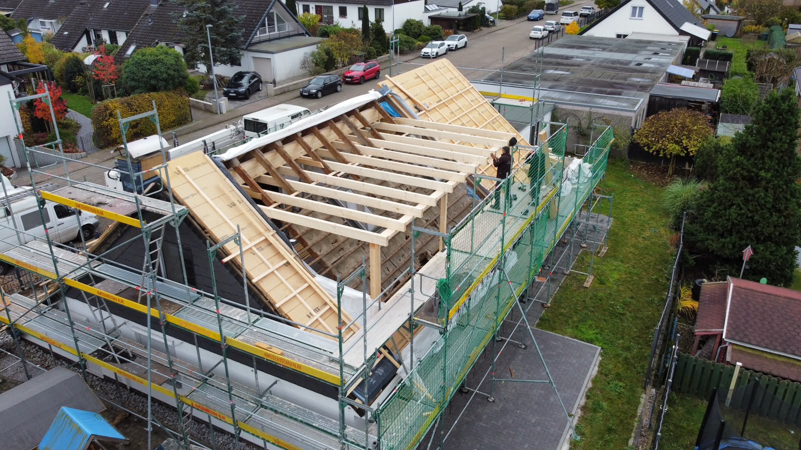 Zwei Dachdecker stellen auf dem Gerüst die Sparren und Pfosten der neuen breiten Dachgaube auf